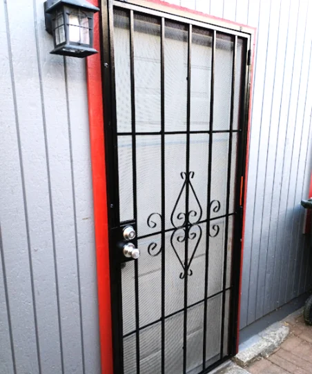 Newly installed black metal security screen door on a home exterior with red trim and grey siding.